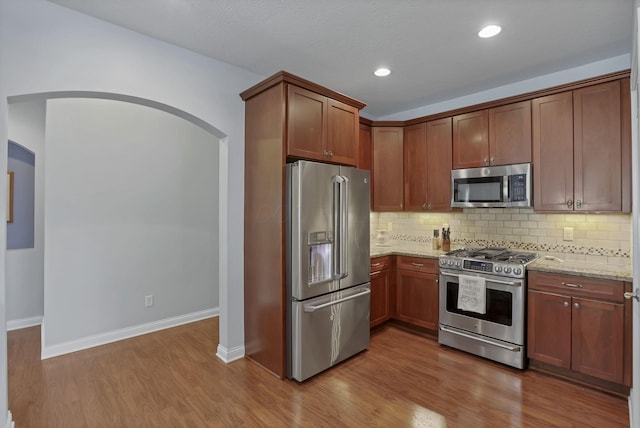 5685 Slater Rdg, Hilliard, OH 43026 - kitchen featuring stainless steel appliances, light stone counters, decorative backsplash, arched walkways, and recessed lighting