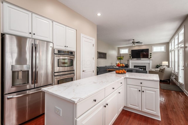 7212 New Albany Links Dr, New Albany, OH 43054 - kitchen featuring stainless steel appliances, ceiling fan, open floor plan, a fireplace, and light stone countertops