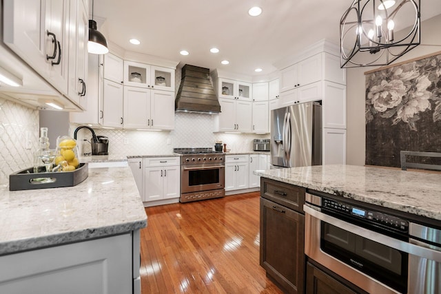 8918 Filiz Ln, Powell, OH 43065 - kitchen with appliances with stainless steel finishes, custom exhaust hood, a chandelier, light wood-style flooring, and white cabinets