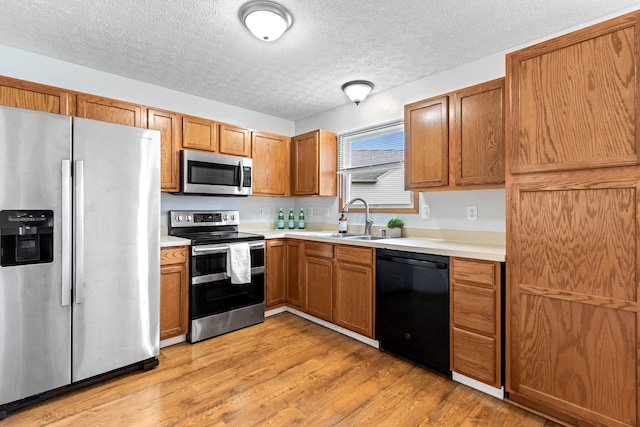 5722 Silver Spurs Ln, Galloway, OH 43119 - kitchen with appliances with stainless steel finishes, light countertops, light wood finished floors, a textured ceiling, and brown cabinetry