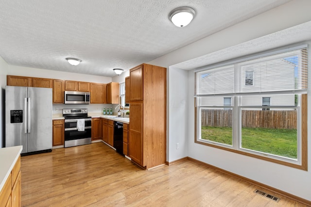 5722 Silver Spurs Ln, Galloway, OH 43119 - kitchen featuring appliances with stainless steel finishes, light countertops, a textured ceiling, light wood-style flooring, and brown cabinetry