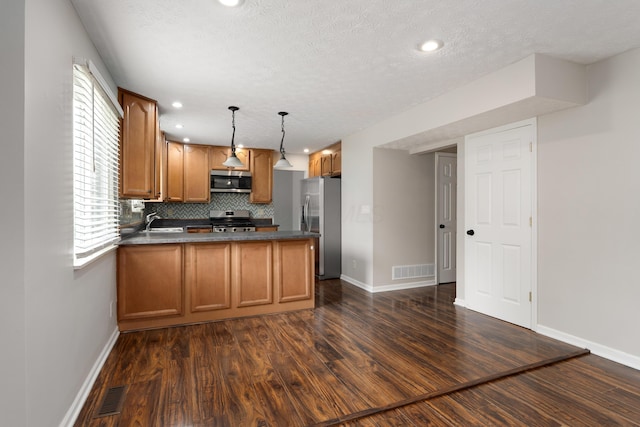 2268 Worthingwoods Blvd, Powell, OH 43065 - kitchen with stainless steel appliances, a peninsula, brown cabinets, dark wood finished floors, and dark countertops