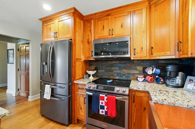 8384 Morris Rd, Hilliard, OH 43026 - kitchen with appliances with stainless steel finishes, light wood finished floors, backsplash, brown cabinetry, and light stone counters