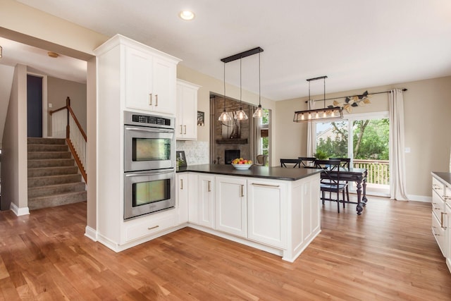 2467 Roe Dr, Lewis Center, OH 43035 - kitchen featuring stainless steel double oven, a peninsula, a fireplace, dark countertops, and decorative backsplash