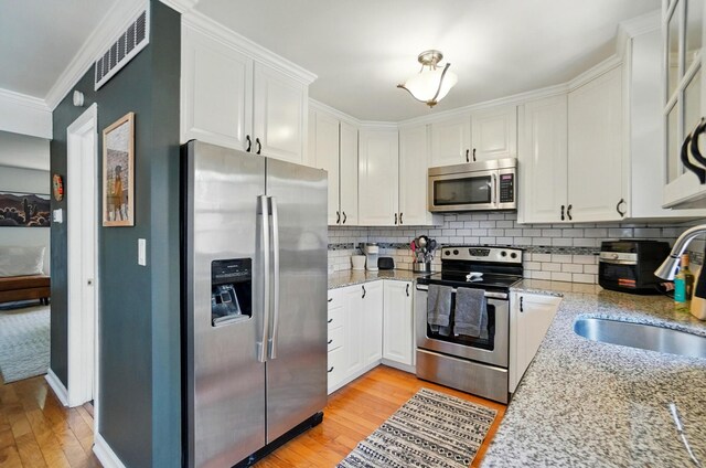 602 Dlyn St Unit H8, Columbus, OH 43228 - kitchen with appliances with stainless steel finishes, light wood-style flooring, white cabinetry, decorative backsplash, and ornamental molding