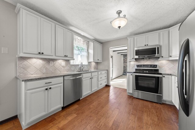 12475 Oak Dr, Orient, OH 43146 - kitchen featuring appliances with stainless steel finishes, wood finished floors, white cabinets, and a textured ceiling