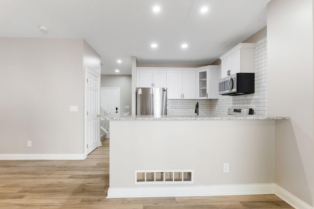 3984 Hill Park Rd, Hilliard, OH 43026 - kitchen with appliances with stainless steel finishes, a peninsula, recessed lighting, light stone counters, and glass insert cabinets