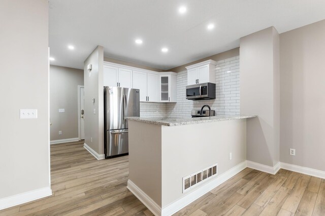 3984 Hill Park Rd, Hilliard, OH 43026 - kitchen featuring stainless steel appliances, a peninsula, white cabinetry, light wood-style flooring, and decorative backsplash