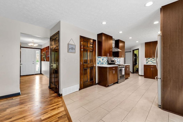 13283 Clover Valley Rd, Croton, OH 43013 - kitchen with appliances with stainless steel finishes, wall chimney range hood, light countertops, a chandelier, and decorative backsplash