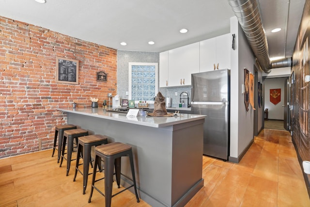 974 N High St Unit B, Columbus, OH 43201 - kitchen featuring freestanding refrigerator, a kitchen bar, a peninsula, white cabinetry, and brick wall