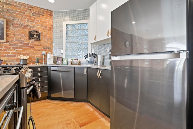 974 N High St Unit B, Columbus, OH 43201 - kitchen featuring stainless steel appliances, white cabinets, brick wall, light countertops, and light wood-style floors