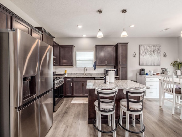 326 Mannaseh Dr W, Granville, OH 43023 - kitchen featuring stainless steel appliances, dark brown cabinets, light wood-type flooring, light stone countertops, and a kitchen island