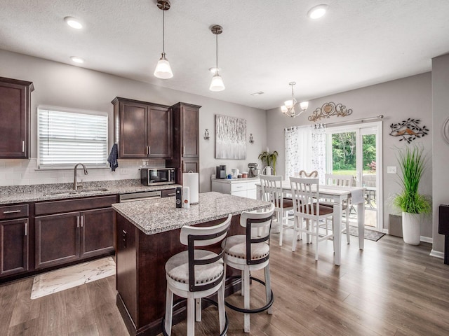 326 Mannaseh Dr W, Granville, OH 43023 - kitchen featuring stainless steel microwave, dark brown cabinets, light stone countertops, wood finished floors, and a kitchen island
