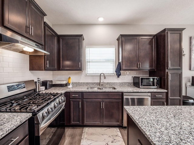 326 Mannaseh Dr W, Granville, OH 43023 - kitchen featuring stainless steel appliances, under cabinet range hood, dark brown cabinetry, light stone countertops, and decorative backsplash