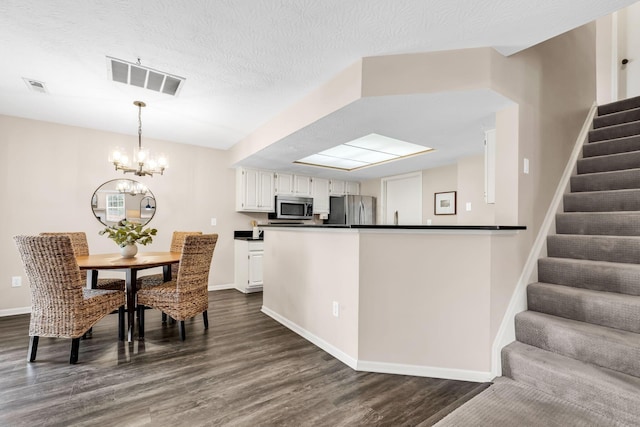 9460 Clermont Cir, Powell, OH 43065 - kitchen with appliances with stainless steel finishes, dark countertops, dark wood-style flooring, a chandelier, and white cabinetry