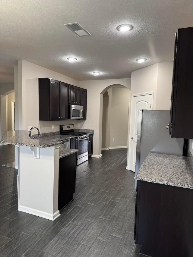 3757 Birkland Cir, Lewis Center, OH 43035 - kitchen featuring appliances with stainless steel finishes, arched walkways, a peninsula, a breakfast bar, and light stone countertops