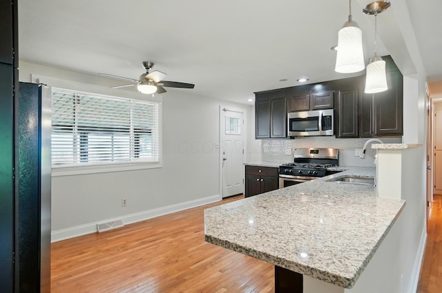 1574 River Bend Rd, Columbus, OH 43223 - kitchen with stainless steel appliances, light wood finished floors, ceiling fan, backsplash, and decorative light fixtures
