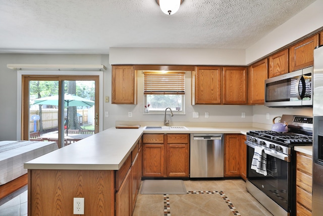 5983 Epernay Way, Galloway, OH 43119 - kitchen with stainless steel appliances, a peninsula, light tile patterned flooring, brown cabinets, and a textured ceiling
