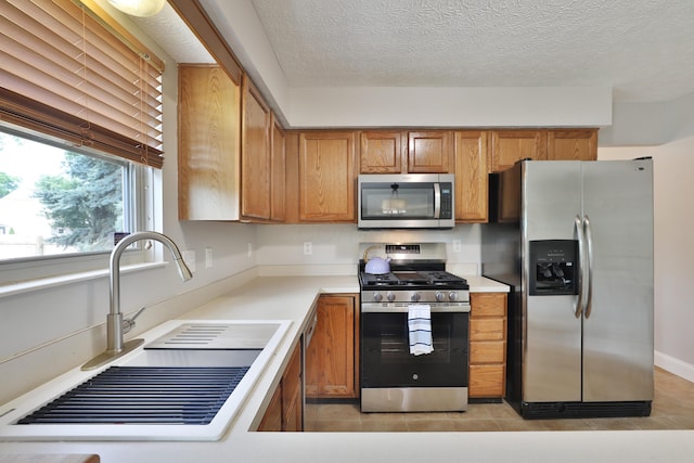 5983 Epernay Way, Galloway, OH 43119 - kitchen featuring appliances with stainless steel finishes, brown cabinetry, light tile patterned floors, light countertops, and a textured ceiling