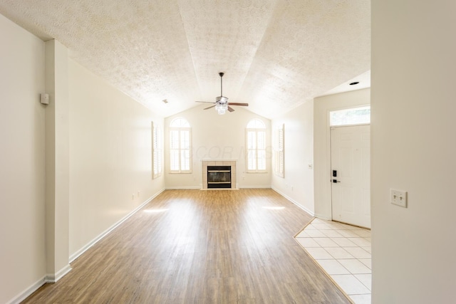 147 Shadymere Ln, Columbus, OH 43213 - unfurnished living room with a ceiling fan, light wood-style flooring, a textured ceiling, a tiled fireplace, and lofted ceiling