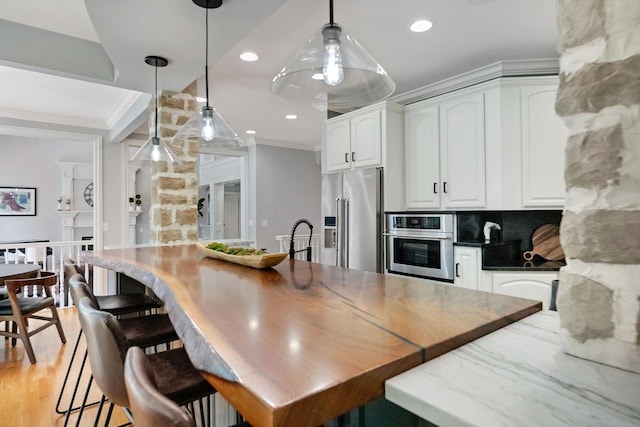 3917 Tarrington Ln, Columbus, OH 43220 - kitchen featuring appliances with stainless steel finishes, white cabinetry, hanging light fixtures, crown molding, and dark stone counters