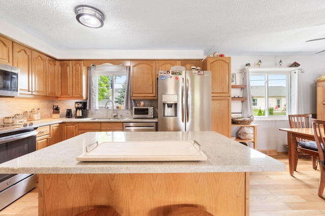 8621 Renford Ct, Powell, OH 43065 - kitchen with appliances with stainless steel finishes, light countertops, a textured ceiling, light wood-style floors, and a kitchen island