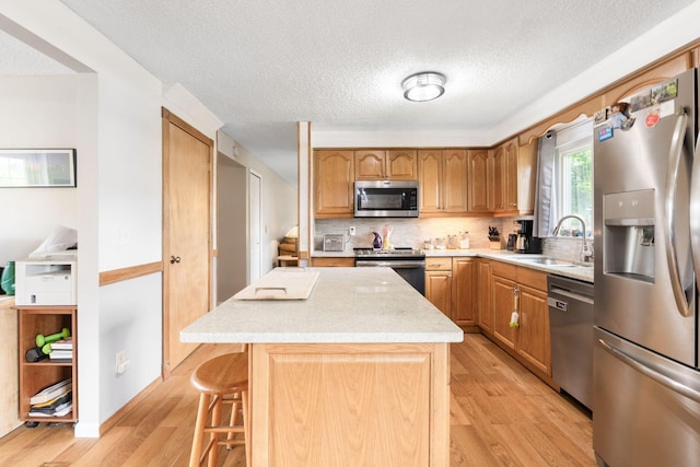8621 Renford Ct, Powell, OH 43065 - kitchen featuring stainless steel appliances, light wood finished floors, a center island, tasteful backsplash, and a kitchen bar
