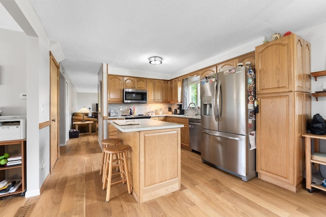 8621 Renford Ct, Powell, OH 43065 - kitchen with stainless steel appliances, a center island, light wood-style flooring, light countertops, and a textured ceiling