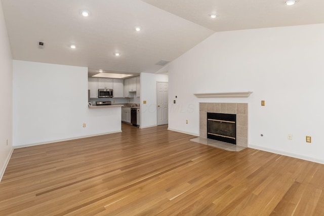 8209 Farm Crossing Cir, Powell, OH 43065 - unfurnished living room with a tiled fireplace, light wood-style flooring, recessed lighting, and lofted ceiling