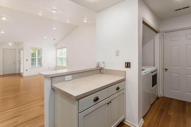 8209 Farm Crossing Cir, Powell, OH 43065 - kitchen with washer and clothes dryer, light wood-style flooring, a peninsula, light countertops, and vaulted ceiling