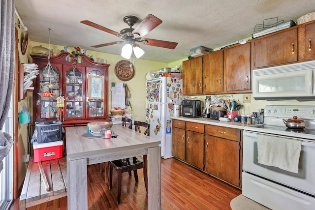 718 Bradwell Dr, Columbus, OH 43207 - kitchen featuring white appliances, wood finished floors, brown cabinetry, a ceiling fan, and a textured ceiling