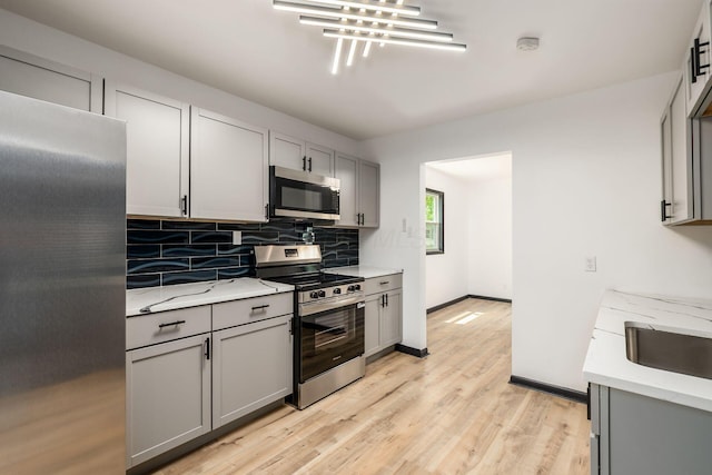 340 Danhurst Rd, Columbus, OH 43228 - kitchen featuring appliances with stainless steel finishes, gray cabinets, decorative backsplash, light wood finished floors, and light stone counters