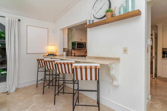233 Preston Rd, Columbus, OH 43209 - kitchen with stainless steel microwave, crown molding, a kitchen bar, decorative backsplash, and light countertops
