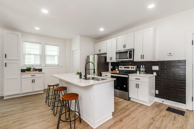 1233 Oakwood Ave, Columbus, OH 43206 - kitchen with appliances with stainless steel finishes, light wood-style floors, a breakfast bar, white cabinetry, and recessed lighting