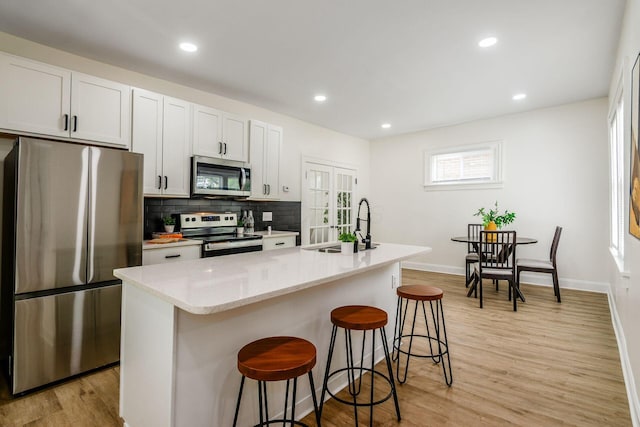 1233 Oakwood Ave, Columbus, OH 43206 - kitchen featuring stainless steel appliances, a breakfast bar area, tasteful backsplash, light wood-style floors, and a center island with sink
