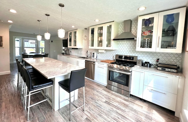 8576 Army Pl, Galloway, OH 43119 - kitchen featuring wall chimney exhaust hood, stainless steel appliances, a kitchen island, white cabinets, and wood finished floors