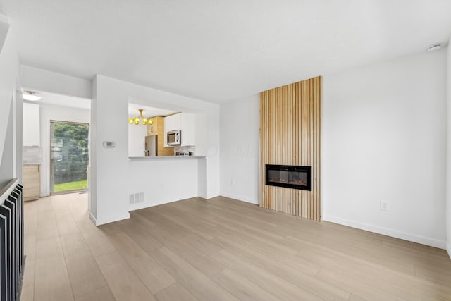 914 Worthington Woods Blvd Unit 11, Columbus, OH 43085 - unfurnished living room featuring a chandelier, light wood-style flooring, and a fireplace