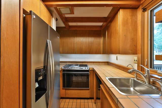 230 E S St, Worthington, OH 43085 - kitchen with appliances with stainless steel finishes, tile counters, plenty of natural light, brown cabinets, and beam ceiling