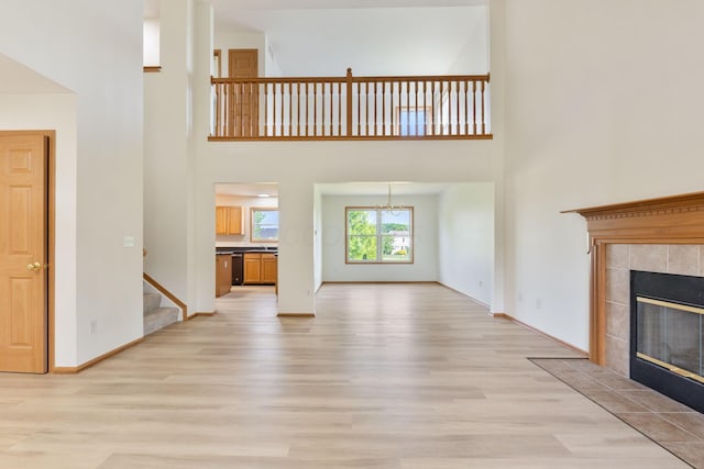 113 Olentangy Meadows Dr, Lewis Center, OH 43035 - unfurnished living room with light wood-type flooring, a towering ceiling, stairs, a tiled fireplace, and a chandelier