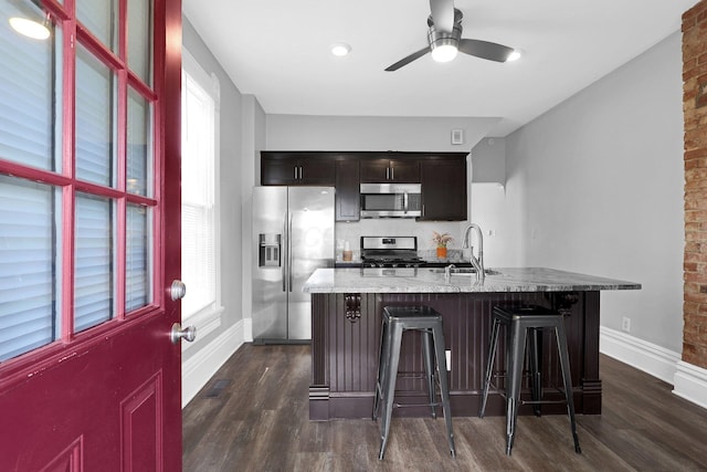611 E 11th Ave, Columbus, OH 43211 - kitchen featuring appliances with stainless steel finishes, dark wood-style floors, a breakfast bar area, a ceiling fan, and brick wall