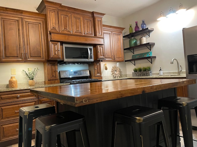 617 E 11th Ave, Columbus, OH 43211 - kitchen with appliances with stainless steel finishes, wood counters, a breakfast bar, and brown cabinetry