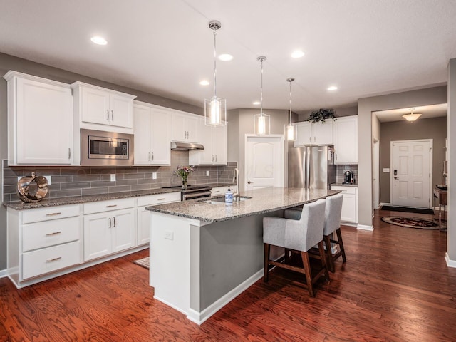 8105 Jitterbug Ln, Pickerington, OH 43147 - kitchen with appliances with stainless steel finishes, under cabinet range hood, a kitchen island with sink, dark wood-style floors, and white cabinets