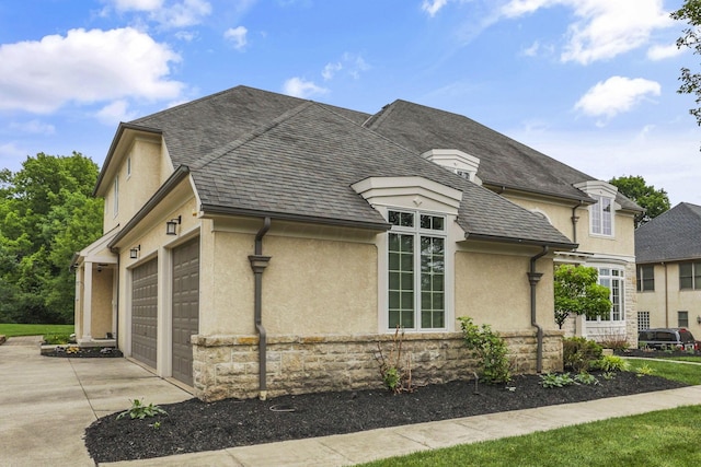 4329 Wyandotte Woods Blvd, Dublin, OH 43016 - view of side of property with stucco siding, driveway, an attached garage, stone siding, and a shingled roof