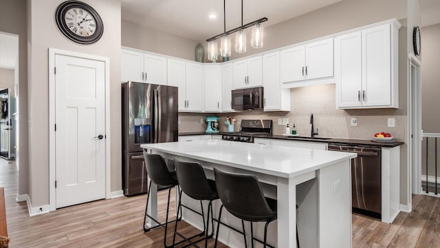 7087 Ribault Dr NW, Pickerington, OH 43147 - kitchen featuring appliances with stainless steel finishes, decorative backsplash, light wood finished floors, white cabinetry, and a kitchen island