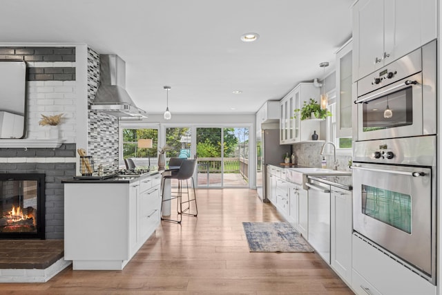 1838 Merriweather Dr, Columbus, OH 43221 - kitchen with wall chimney exhaust hood, stainless steel appliances, backsplash, white cabinetry, and a brick fireplace
