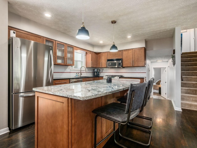 5247 Heathmoor St, Columbus, OH 43235 - kitchen featuring stainless steel appliances, brown cabinetry, dark wood-type flooring, light stone countertops, and a center island