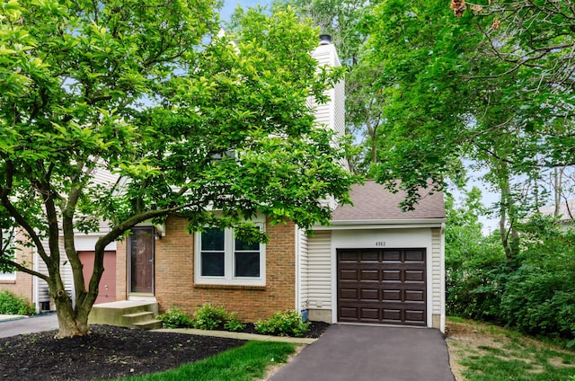 4963 Buck Thorn Ln, Columbus, OH 43220 - view of property hidden behind natural elements with asphalt driveway, brick siding, a chimney, and a shingled roof