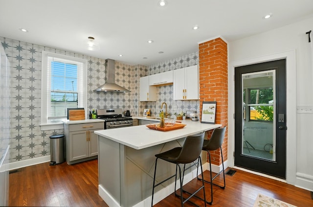 484 Sheldon Ave, Columbus, OH 43207 - kitchen featuring wall chimney exhaust hood, gas range, a kitchen bar, dark wood-style flooring, and light countertops
