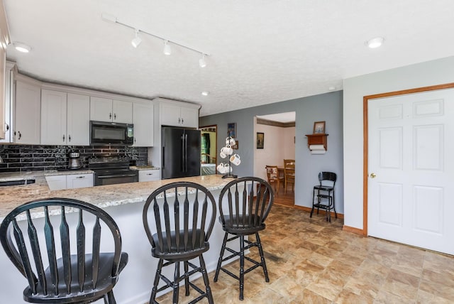 51801 State Route 671, Londonderry, OH 45647 - kitchen with black appliances, a kitchen bar, decorative backsplash, light stone countertops, and a peninsula