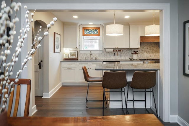 678 S Cassingham Rd, Columbus, OH 43209 - kitchen featuring a kitchen breakfast bar, tasteful backsplash, dark wood-style flooring, white cabinets, and hanging light fixtures